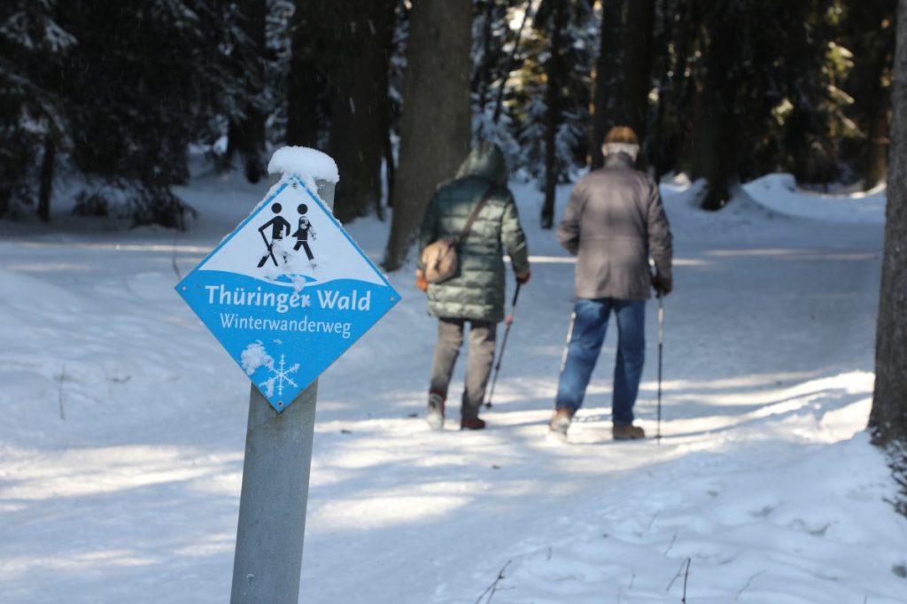 Zwei Spaziergänger laufen auf einem schneebedecktem Winterwanderweg durch den Thüringer Wald.